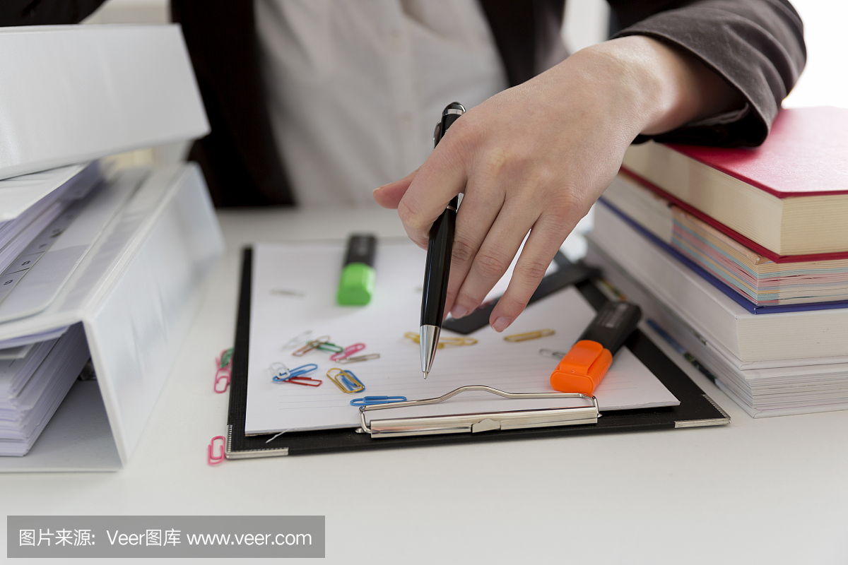 坐在滿是文書,書籍和文件的桌子旁的女人?；靵y的工作場所。過載和過度勞累